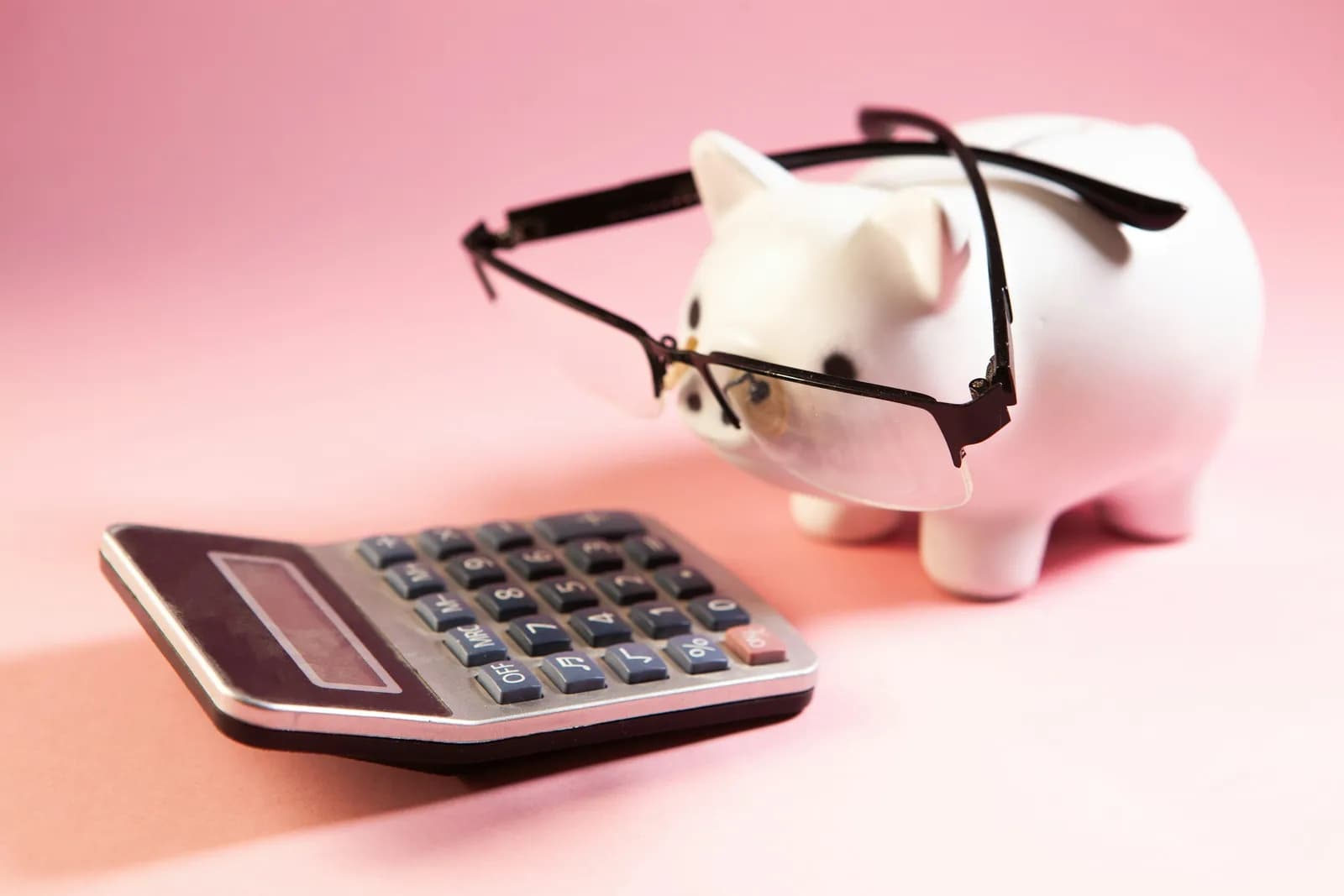 Cofrinho de porquinho com óculos ao lado de uma calculadora