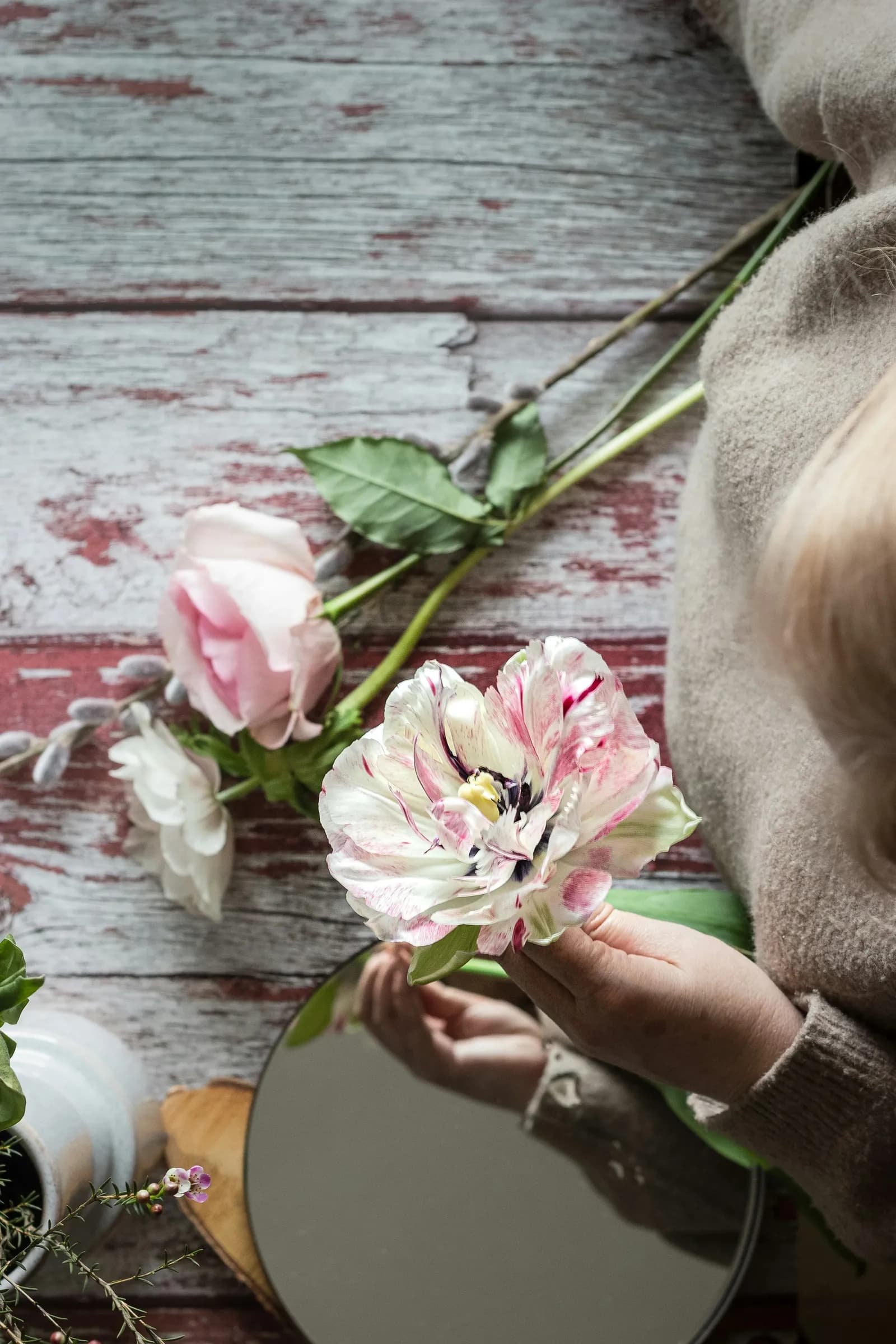 Mãos montando um arranjo de flores sobre uma mesa de madeira