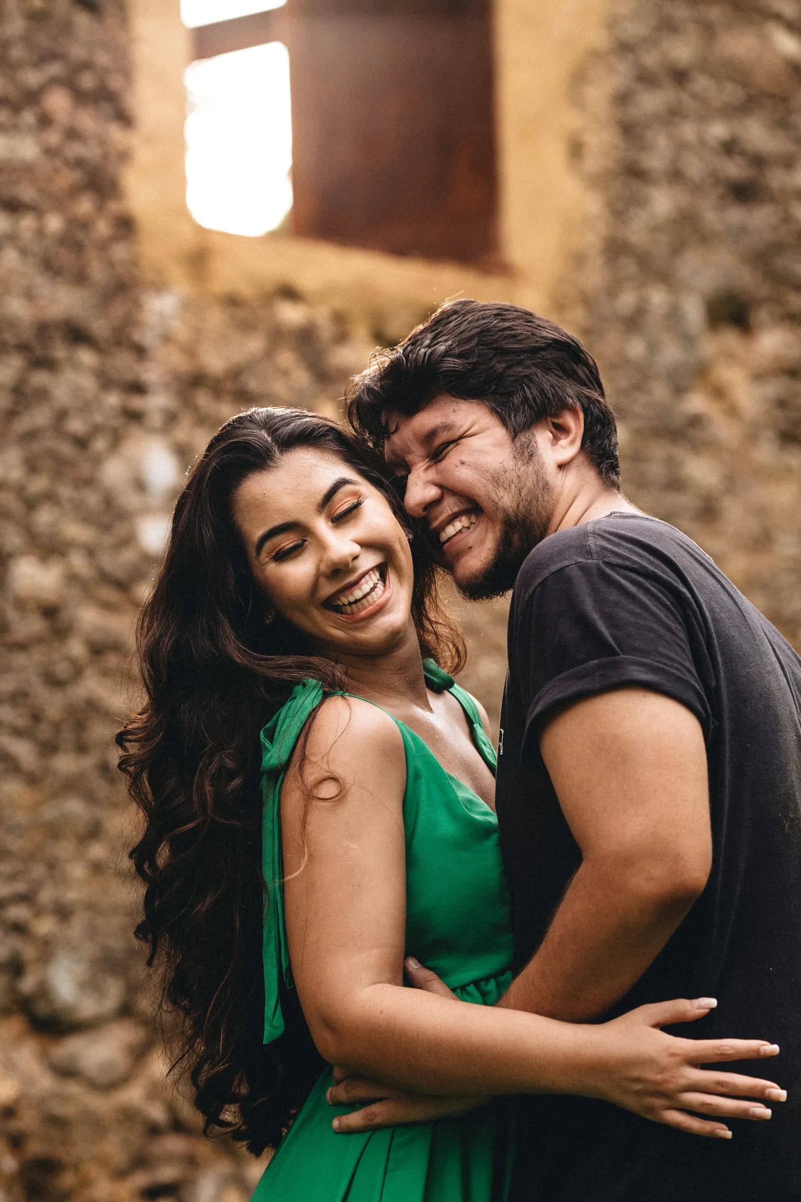 Casal rindo abraçado diante de uma parede de pedra