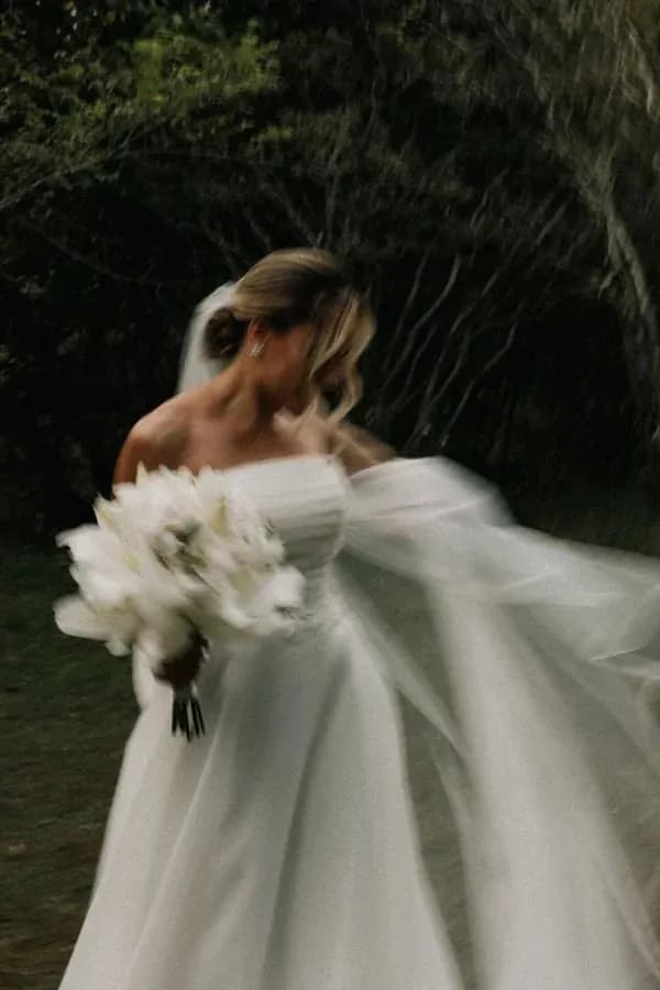 Noiva de vestido branco com buquê, com o véu ao vento
