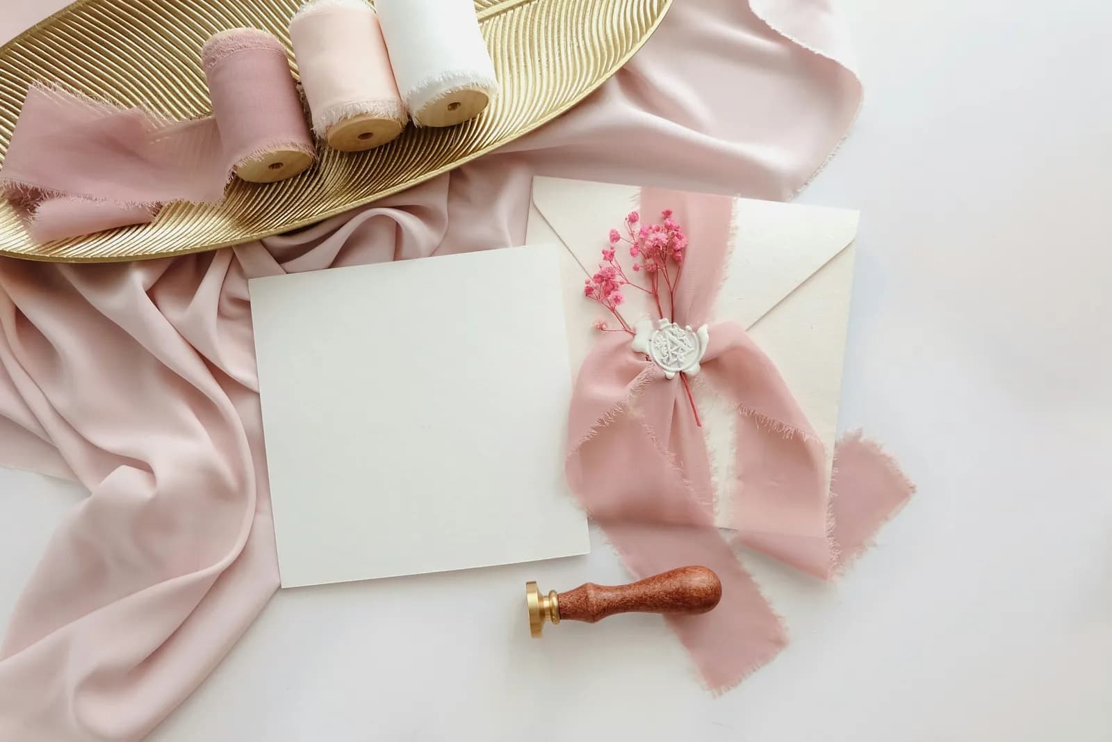 Convite em branco com fita rosa e lacre sobre tecido rosado
