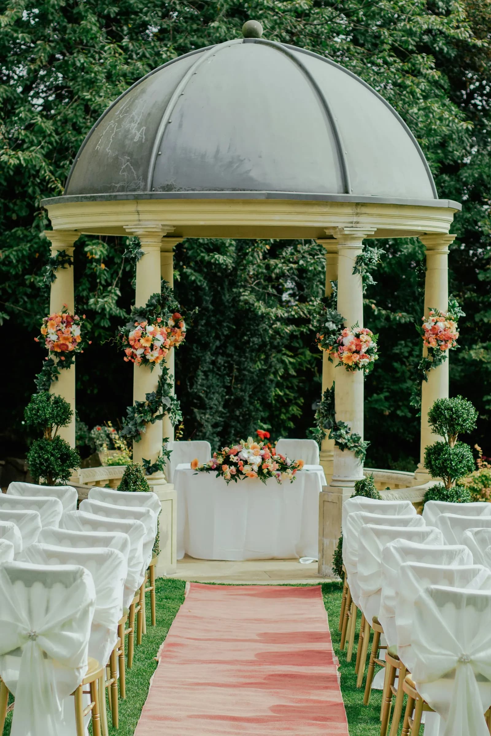 Coreto de jardim com flores e cadeiras brancas ao longo do corredor